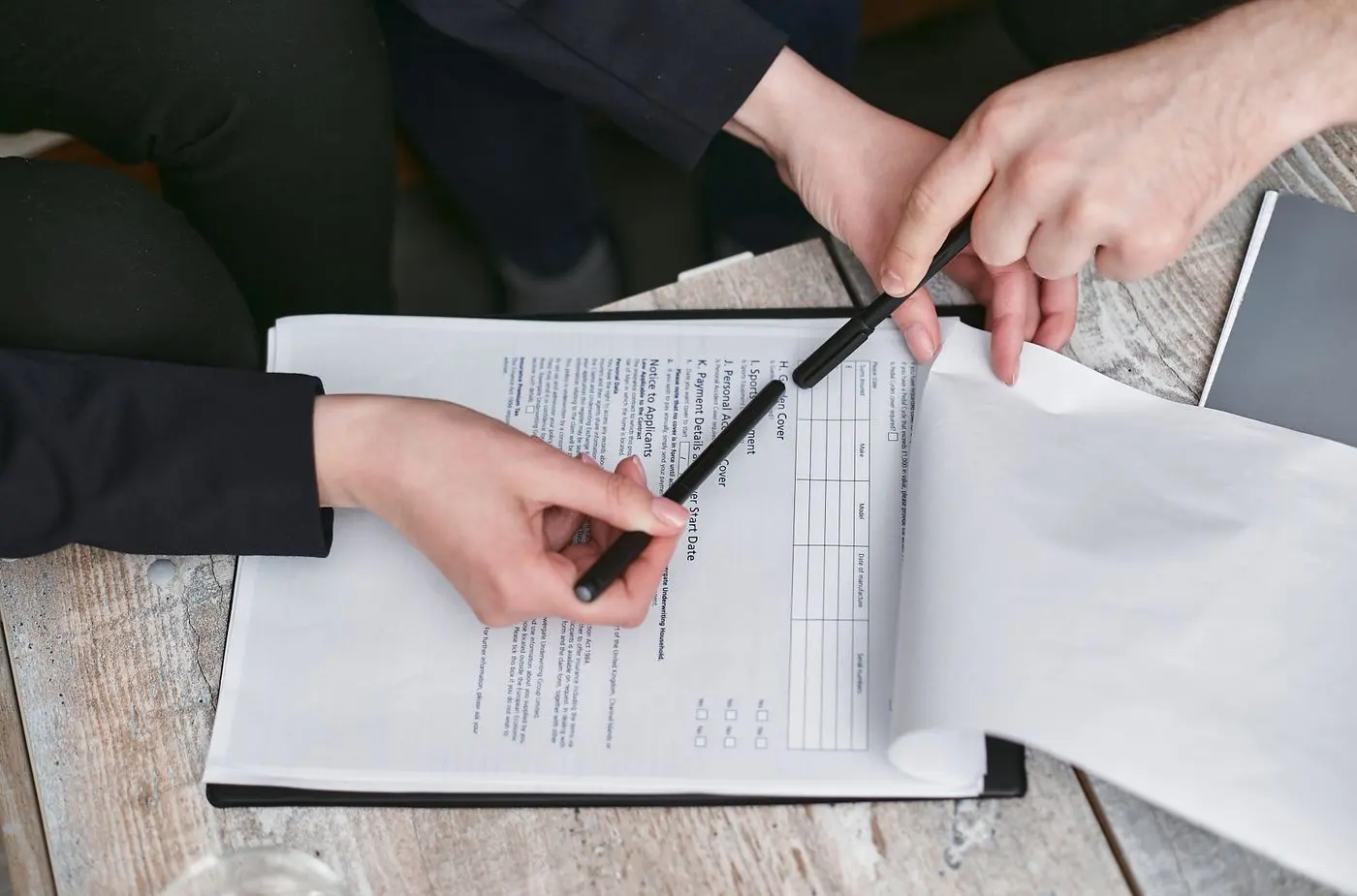 Două persoane semnează un document, cu pixul pe pagină